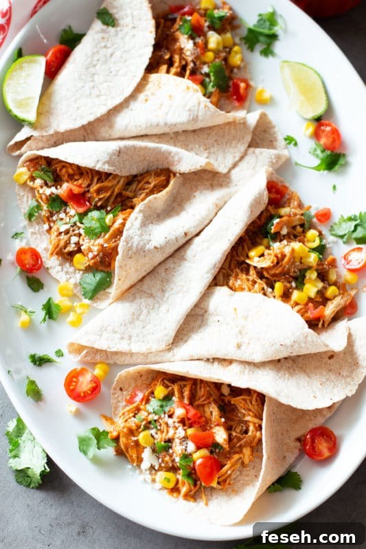 4 soft corn taco shells filled with shredded chicken, topped with cilantro, corn, and cheese.