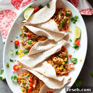 4 tacos filled with shredded salsa chicken, lime and salsa on plate.