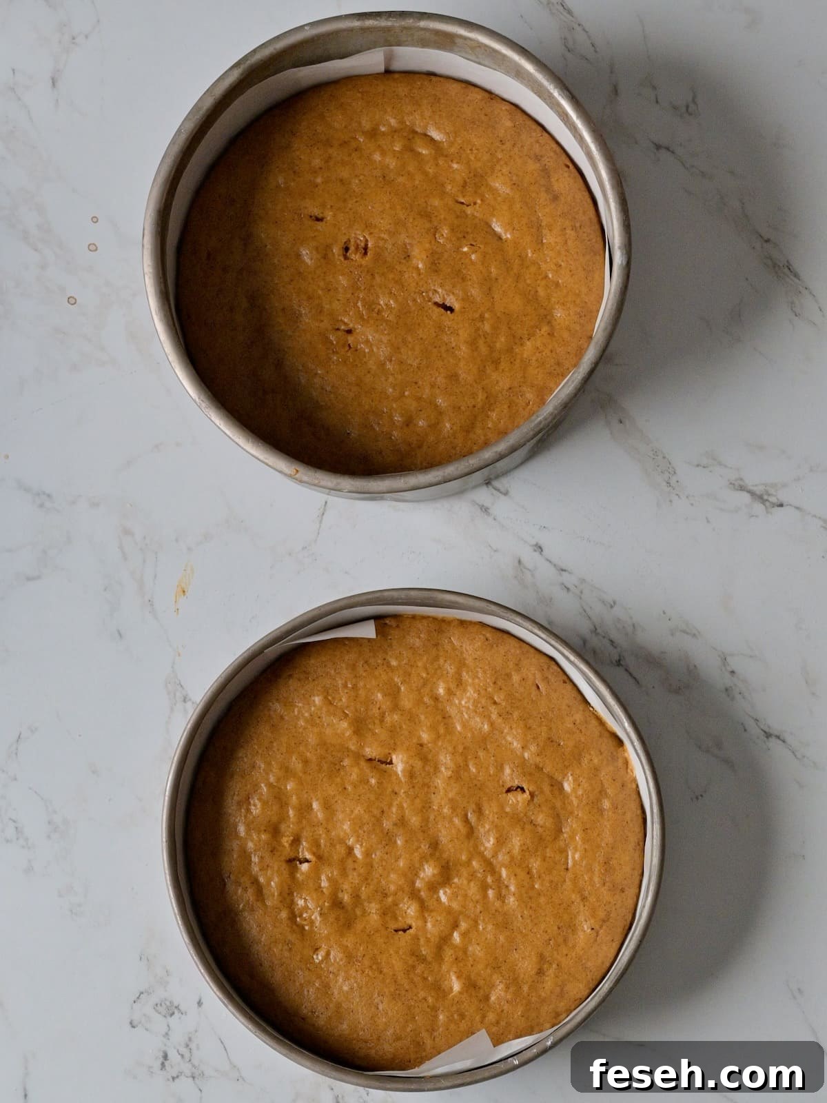 Two freshly baked pumpkin cake layers cooling in their pans.