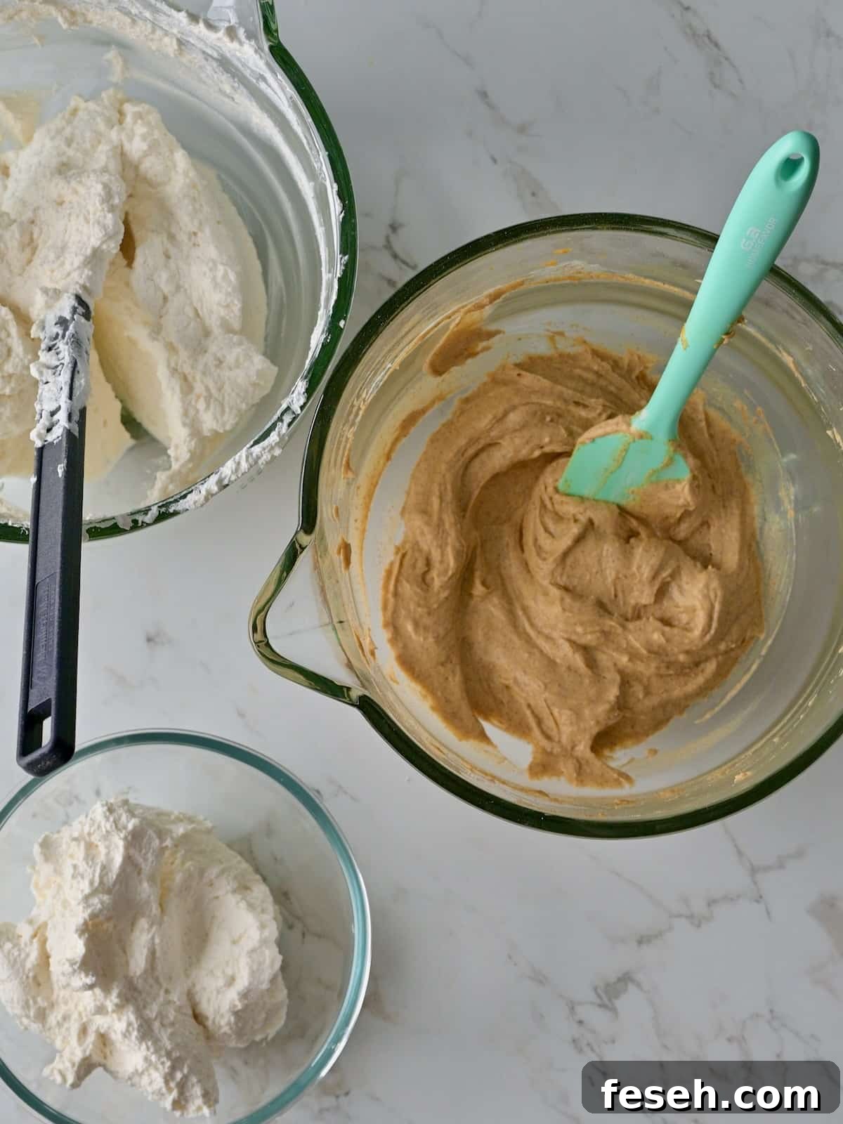 Two bowls of whipped cream next to a bowl of pumpkin mousse base, showing the reserved portions for mousse and frosting the pumpkin cake cheesecake.