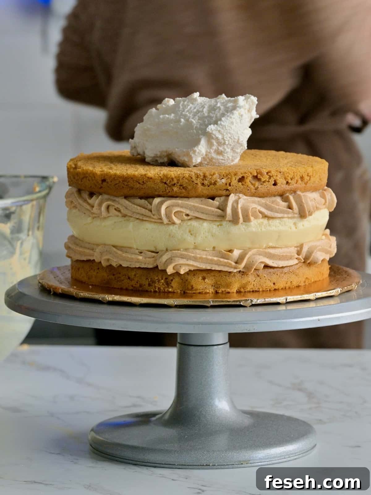 Pumpkin cake cheesecake being assembled with two pumpkin spice cake layers, a cheesecake center, and piped pumpkin mousse filling between each layer.