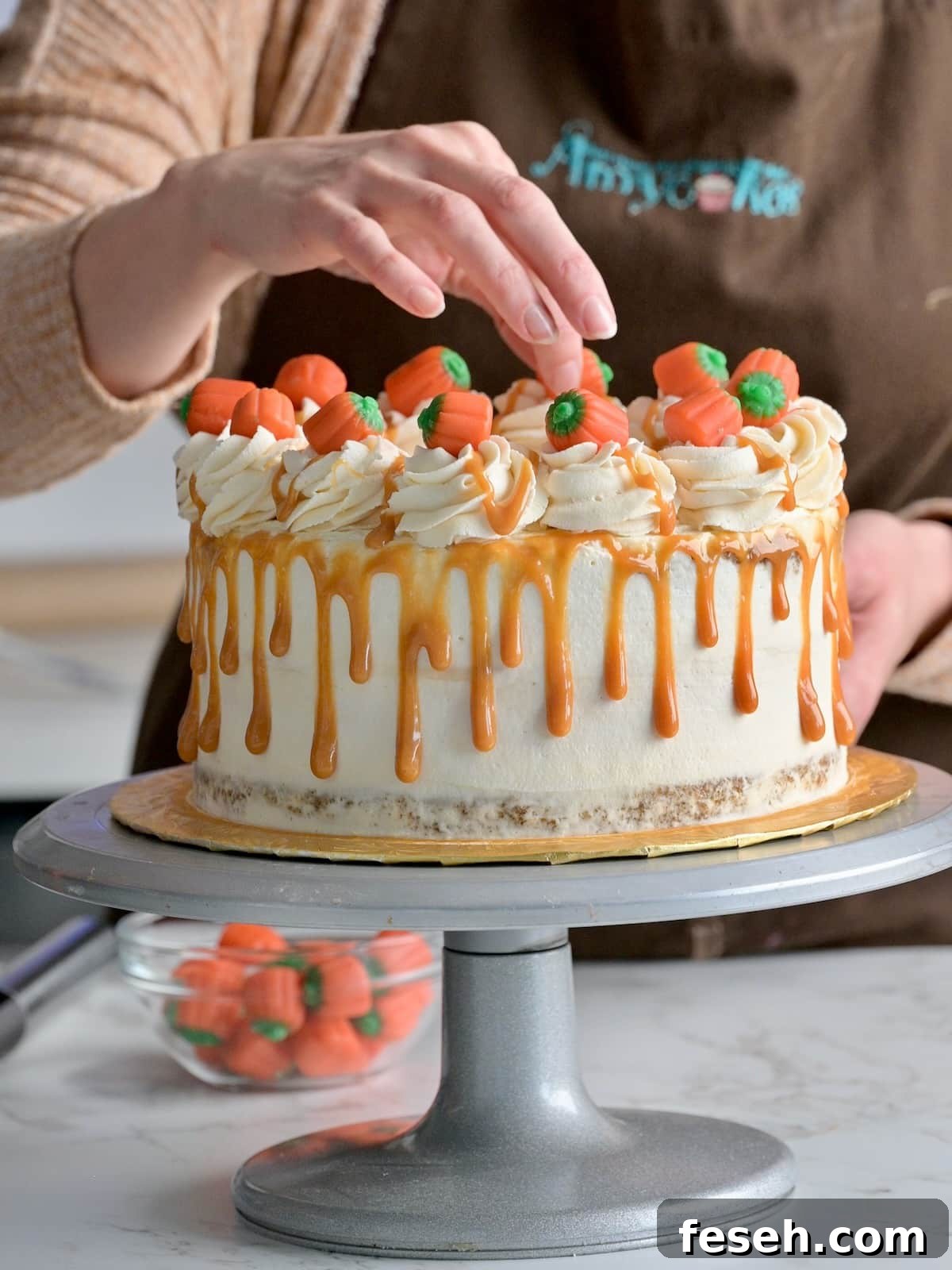 Candy pumpkins being placed on top of a finished pumpkin cheesecake layer cake.