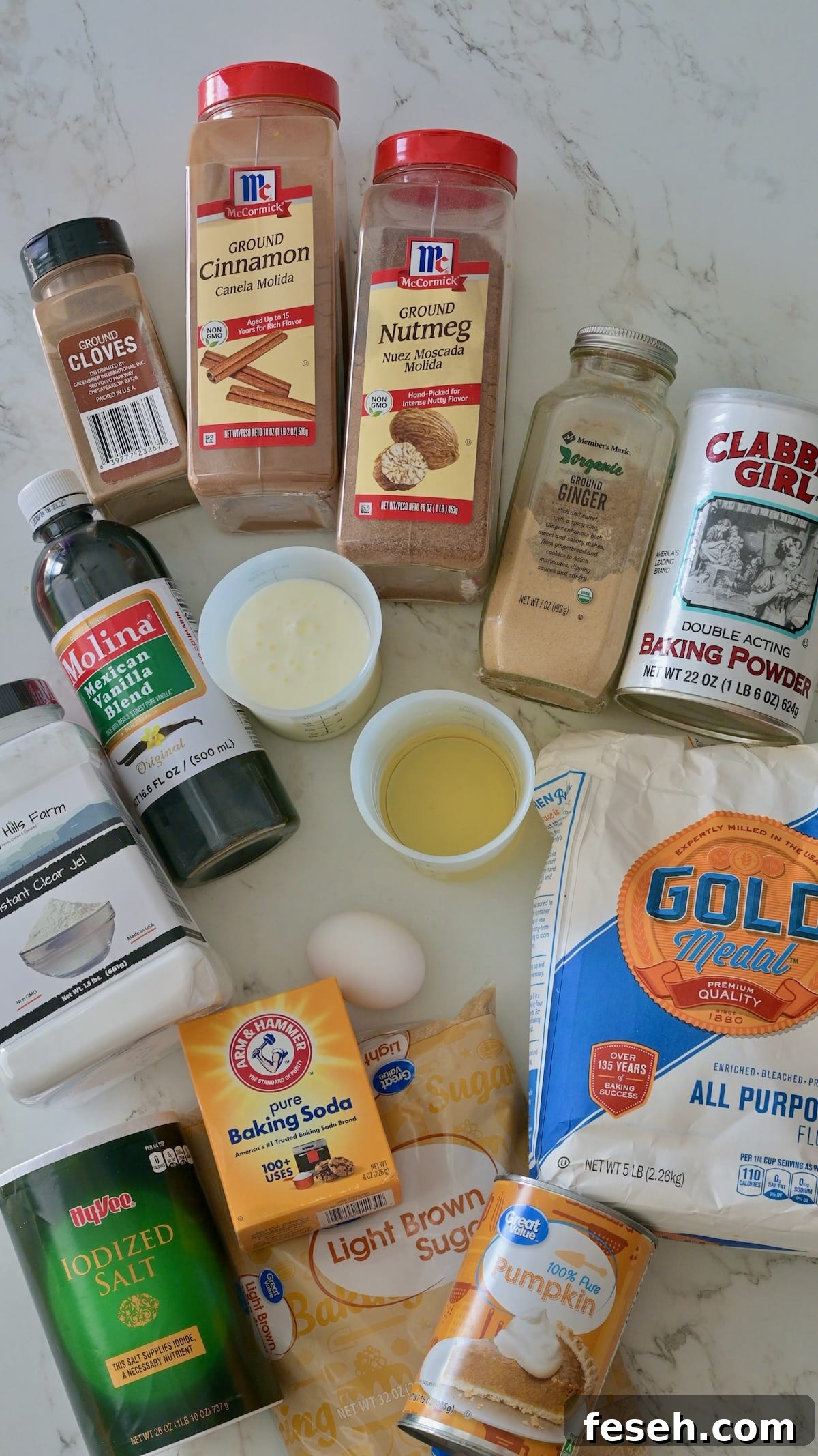 Ingredients for the pumpkin cake layers displayed on a marble surface, including flour, brown sugar, pumpkin purée, baking powder, baking soda, cinnamon, nutmeg, ginger, cloves, vanilla, buttermilk, and vegetable oil.