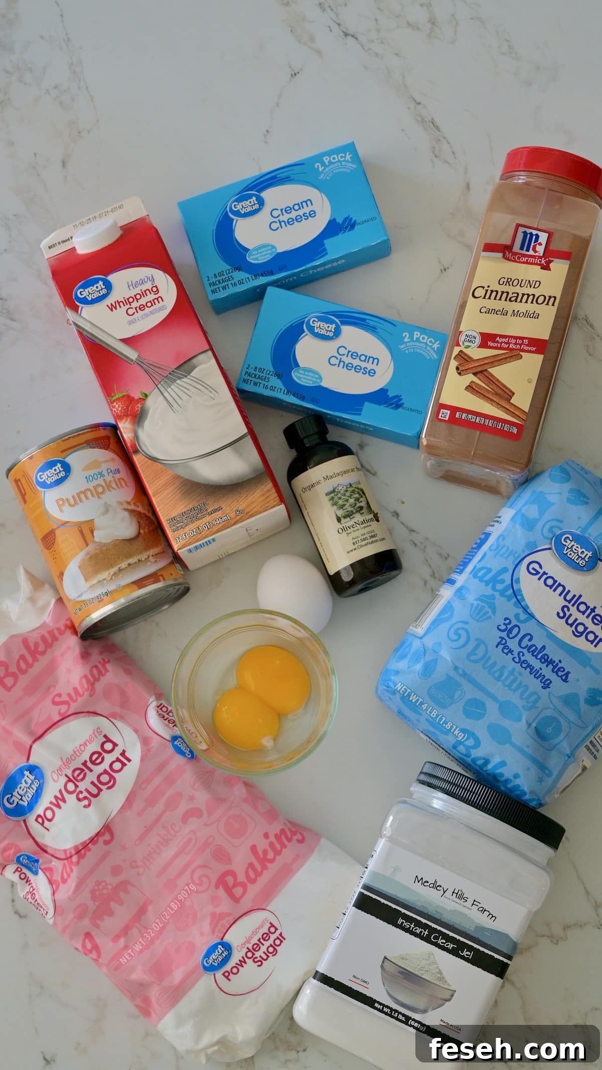 Ingredients for the cheesecake and the pumpkin cream cheese mousse and whipped cream, including cream cheese, heavy whipping cream, powdered sugar, canned pumpkin, eggs, vanilla, and cinnamon on a marble countertop.