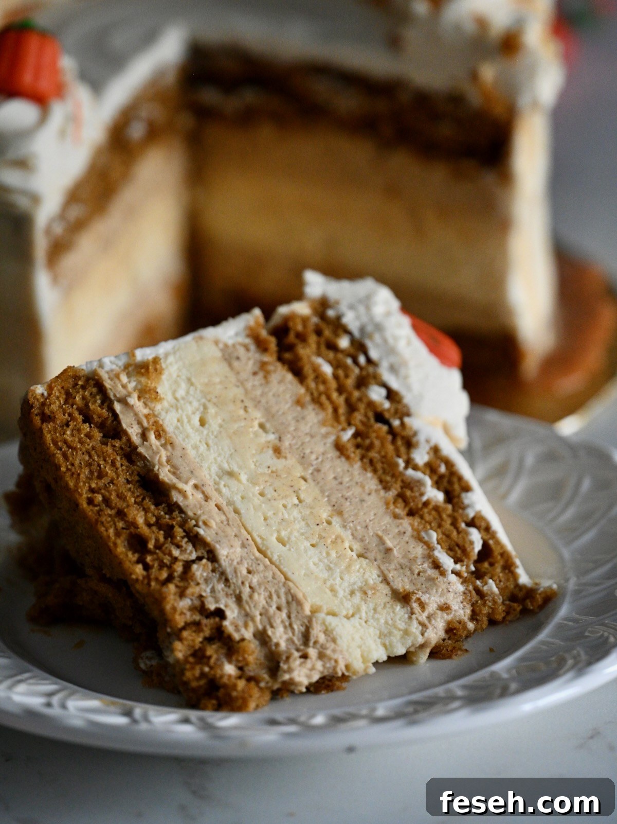 A close-up of a thick slice of pumpkin cake cheesecake showing moist cake and cheesecake layers with whipped frosting and caramel drizzle.