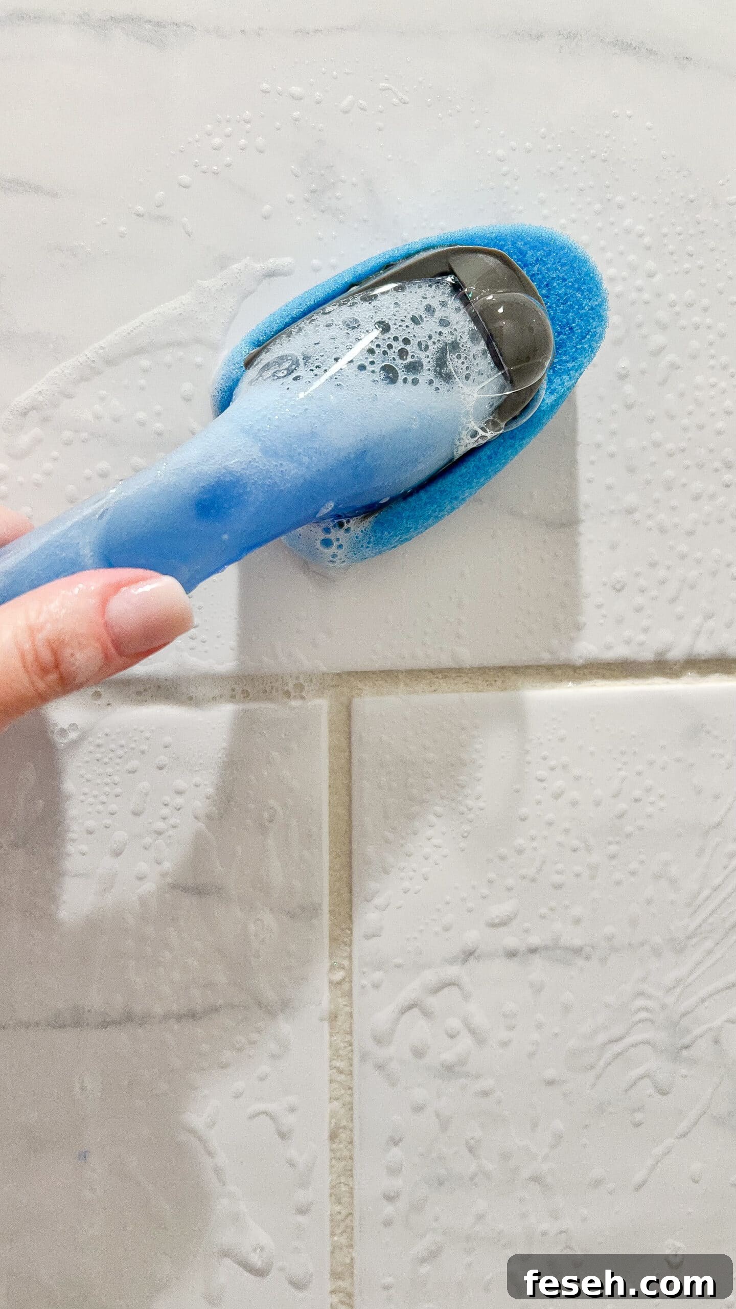 hand holding homemade shower cleaner cleaning shower tiles