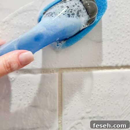 hand holding homemade shower cleaner cleaning shower tiles