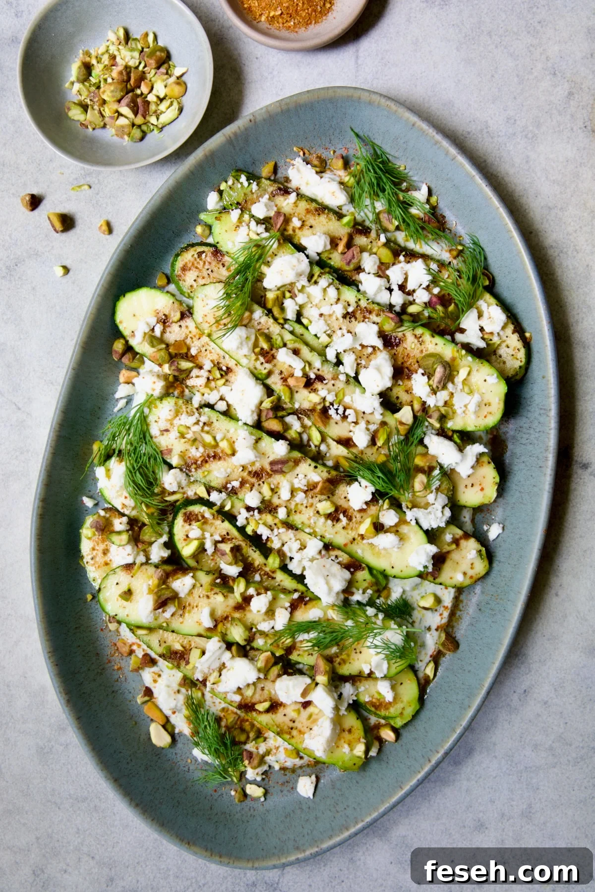 Mediterranean Grilled Zucchini with Dill Yogurt and Feta on blue platter garnished with pistachios and fresh dill sprigs.
