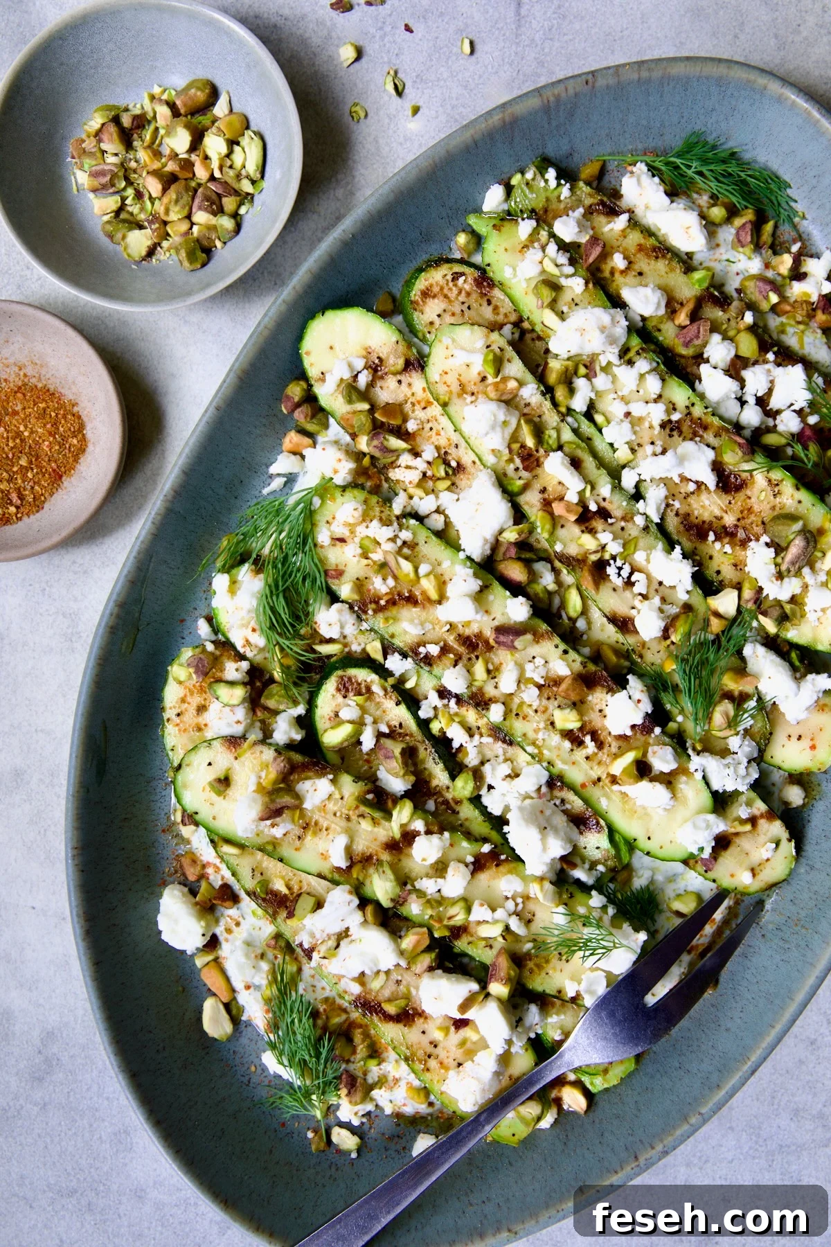 Mediterranean Grilled Zucchini with Dill Yogurt and Feta on blue platter garnished with pistachios and fresh dill sprigs.