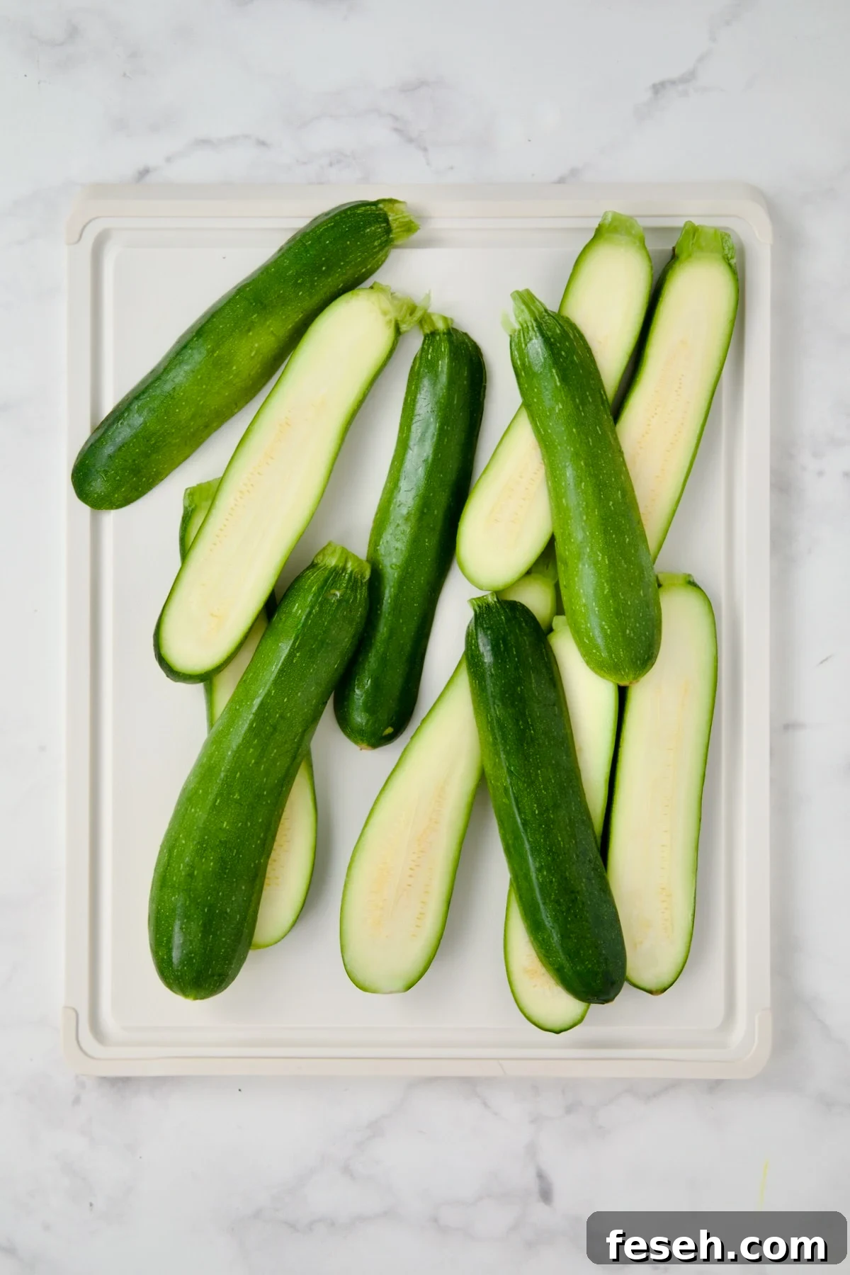 Sliced zucchini on white plastic cutting board.