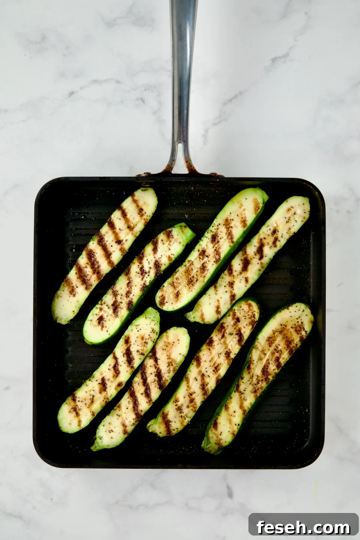 Eight grilled zucchini slices on square grill pan.