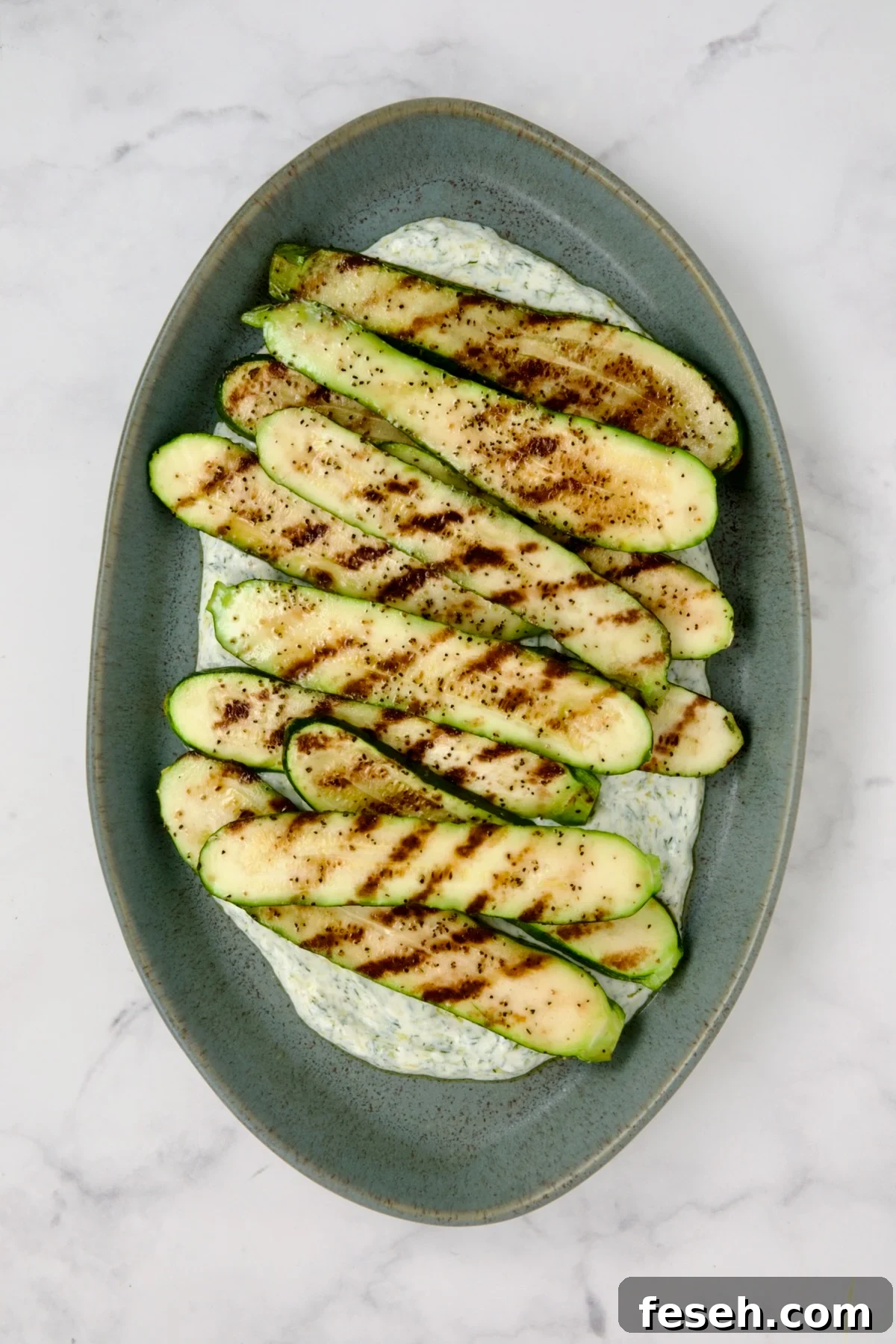 Grilled zucchini slices placed over dill yogurt on blue platter.