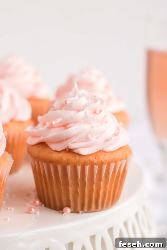 Pink Champagne Cupcake on a Cake stand with a glass of pink champagne behind it. 