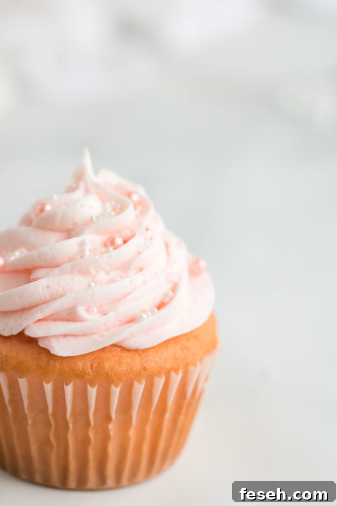 A close up of a pink champagne cupcake with white and pearl sprinkles. 