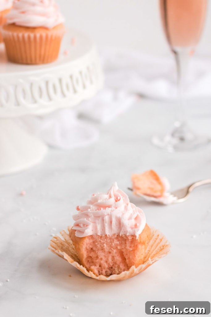 A pink champagne cupcake with a bite out of it and a fork behind it. 