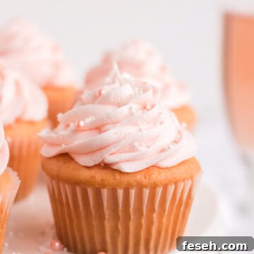Pink champagne cupcake on a white cake stand with a glass of pink champagne behind it.