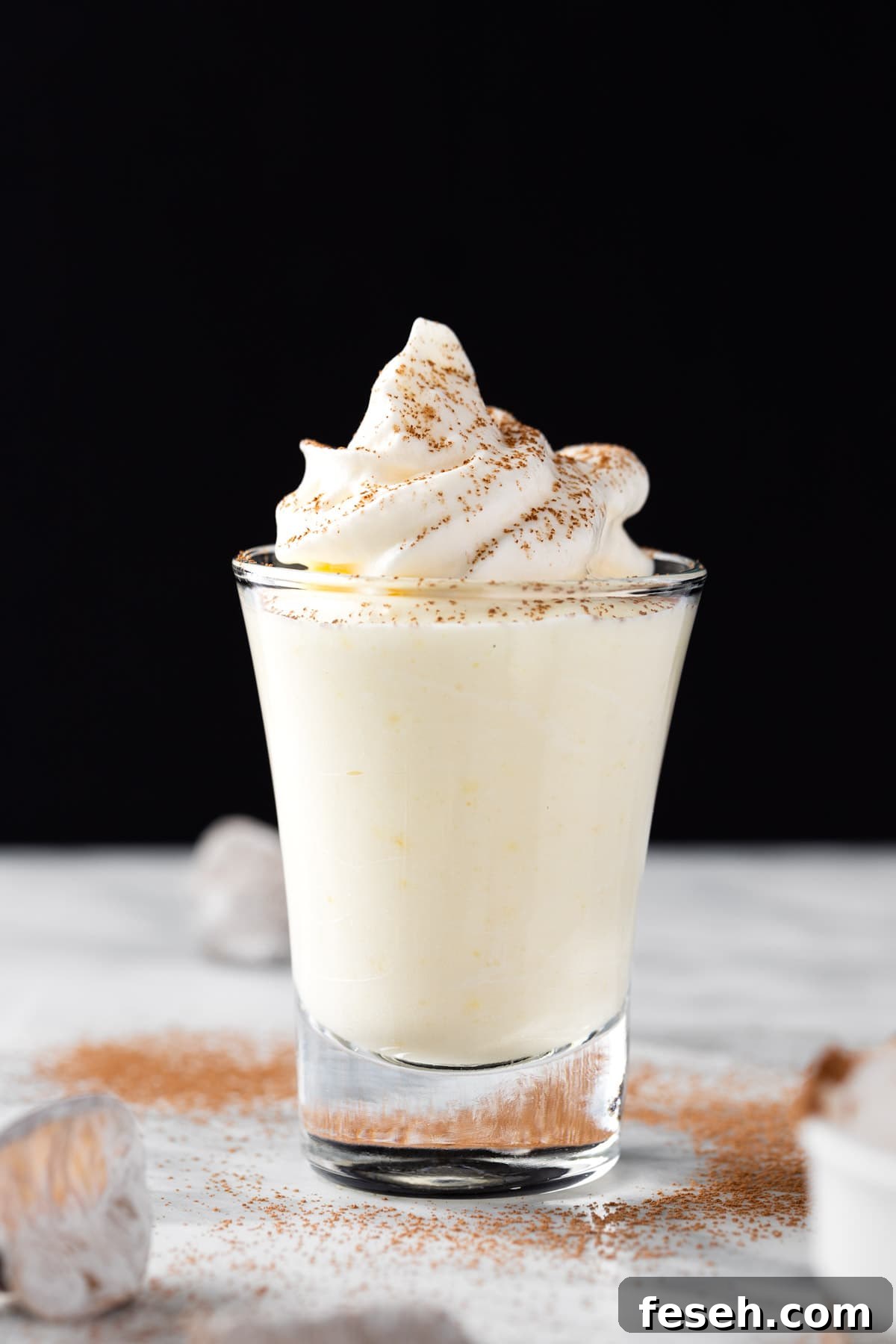 Vanilla pudding shots topped with whipped cream, on a black background.