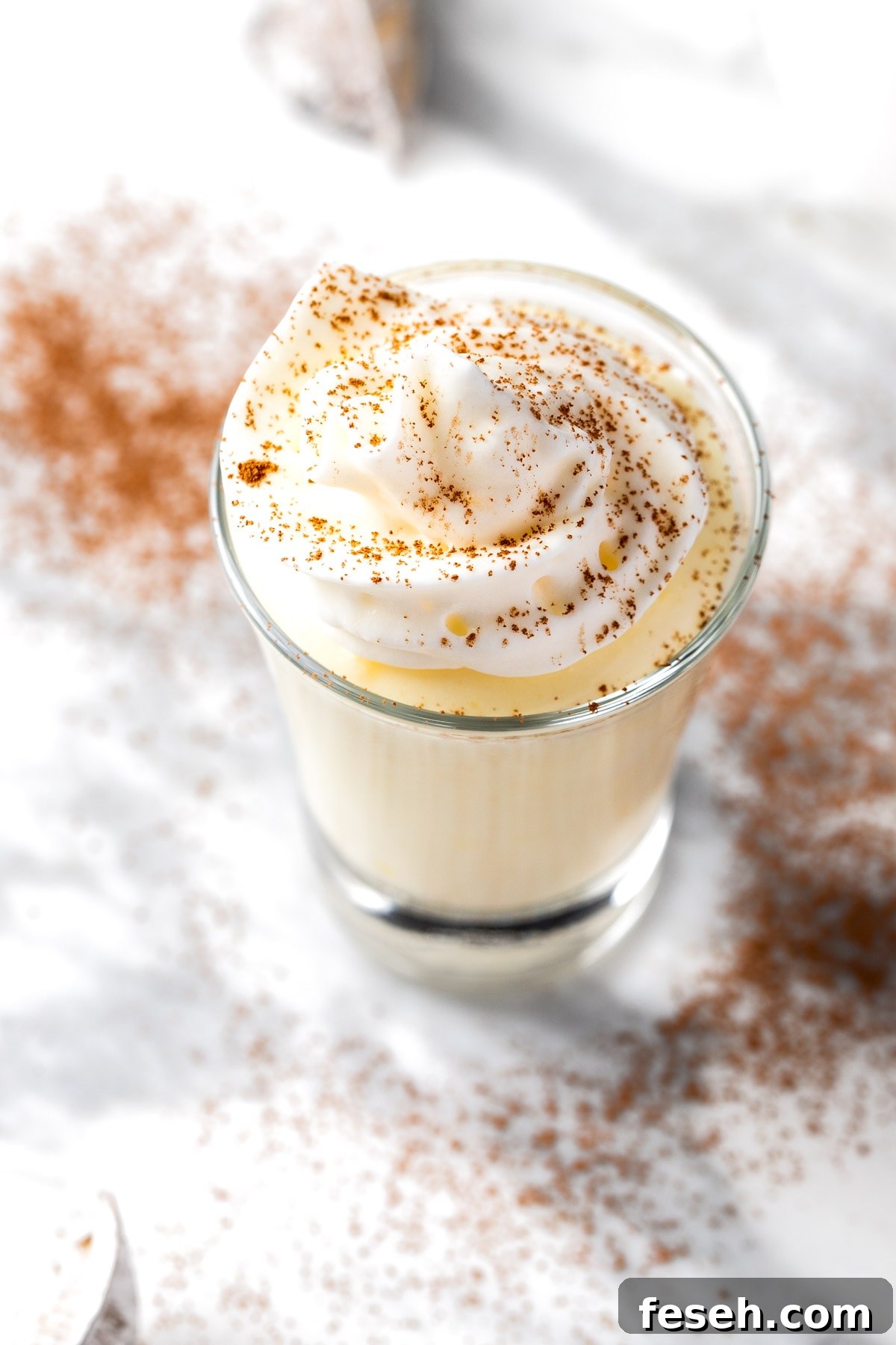 A vodka vanilla pudding shot topped with whipped cream and a sprinkle of cocoa powder.