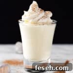 Vanilla pudding shots topped with whipped cream, on a black background.