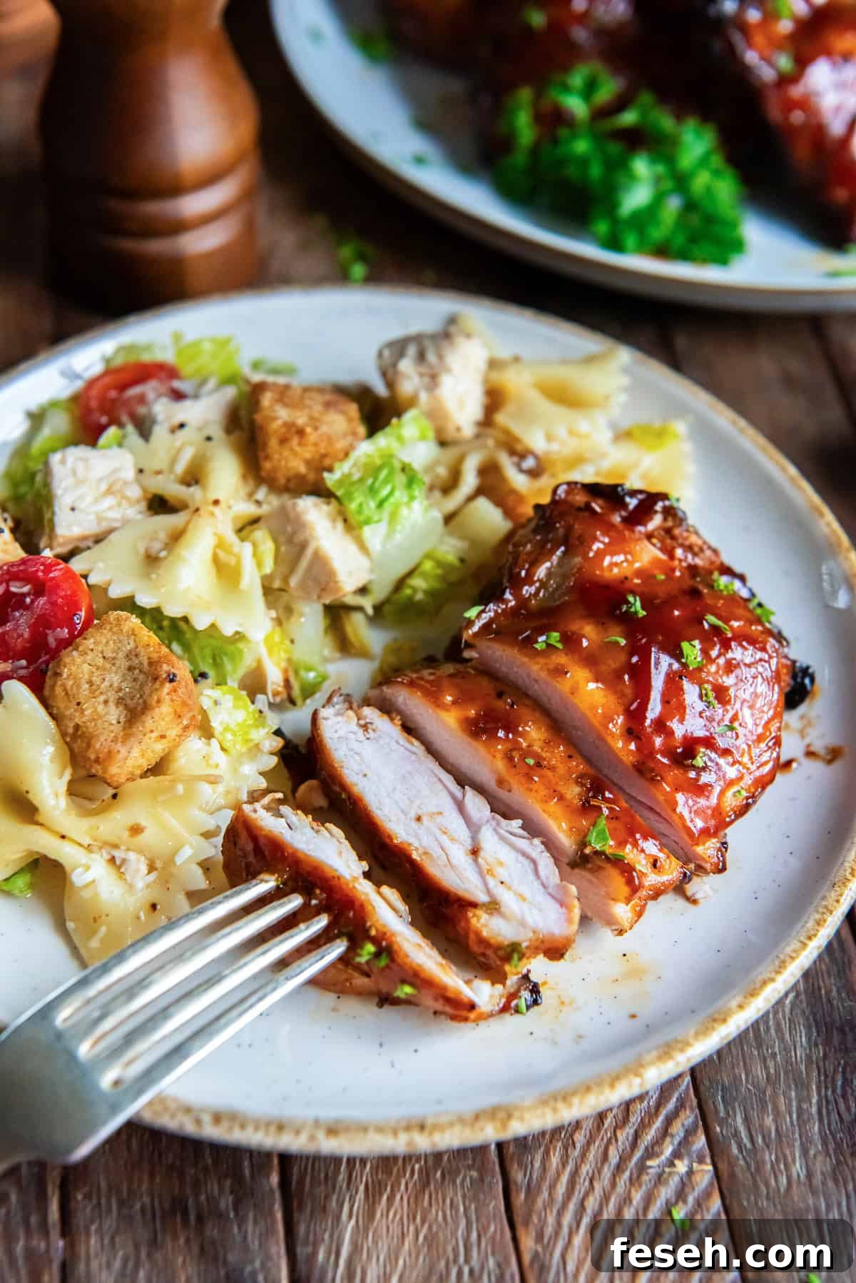 A sliced grilled chicken thigh on a white plate with pasta salad.