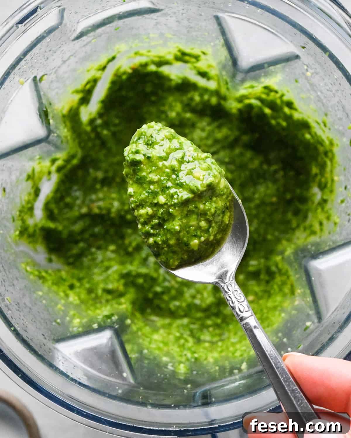 a spoon holding a scoop of pesto sauce over pesto sauce in a blending container to make pesto pasta