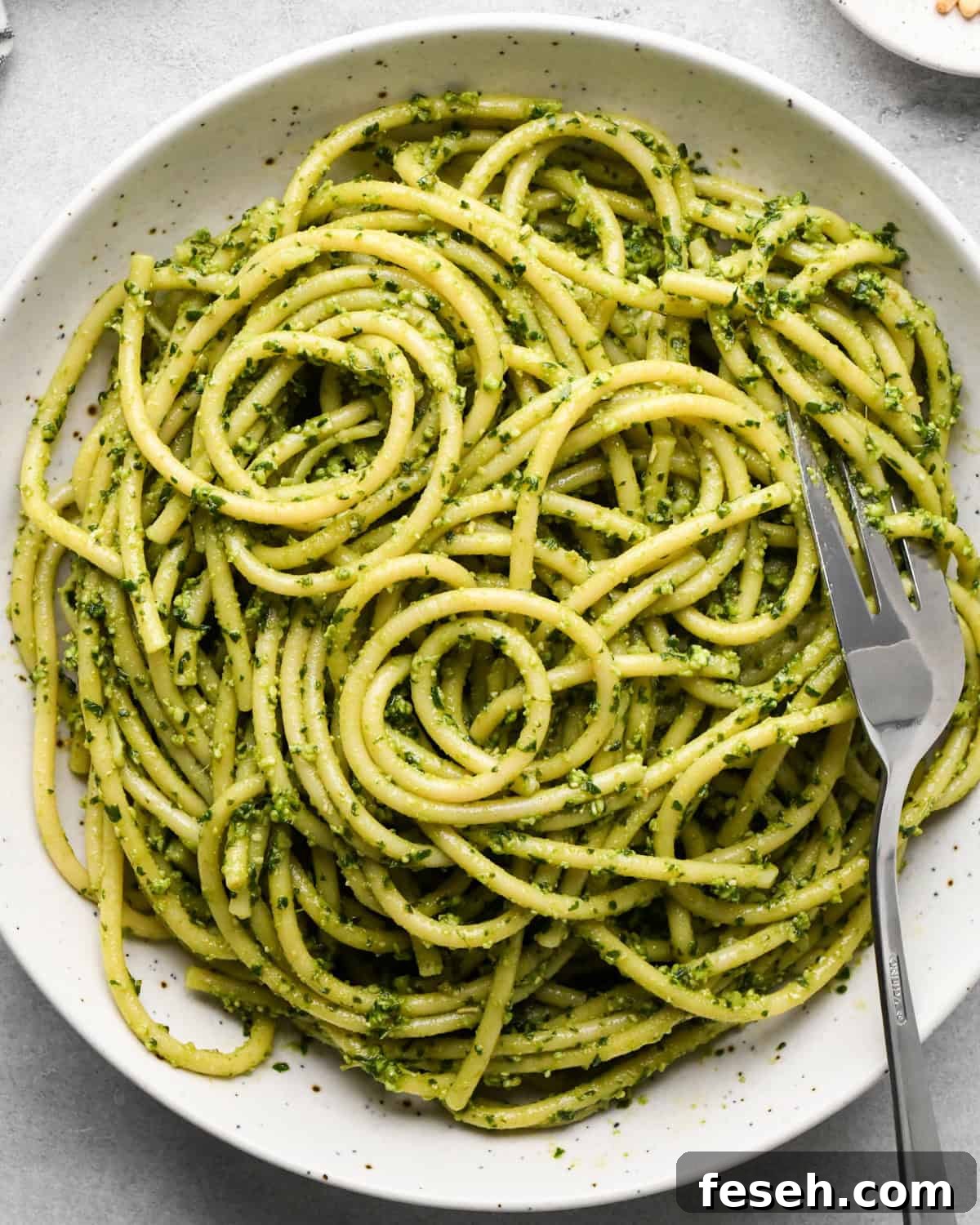 pesto pasta after sauce and noodles have been combined in a white bowl with a silver fork on a gray surface