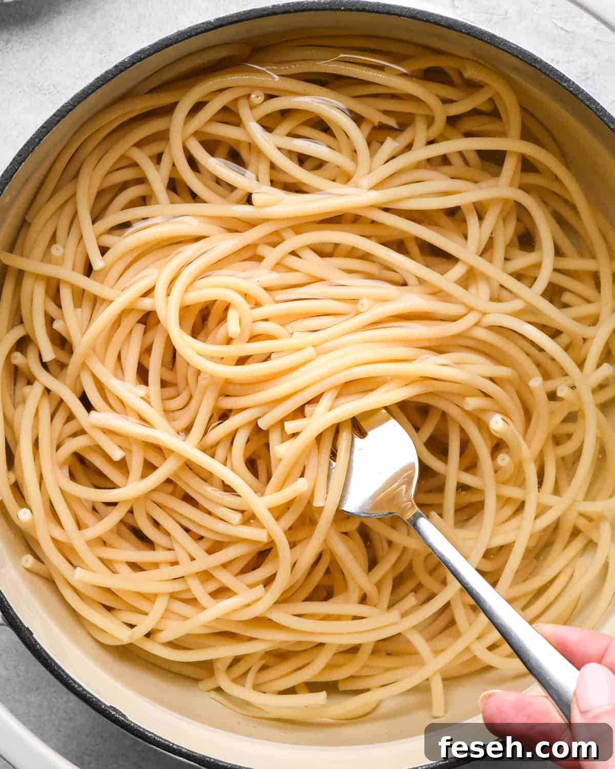 cooked pasta in a pot of water with a fork showing the cooked noodles making pesto pasta