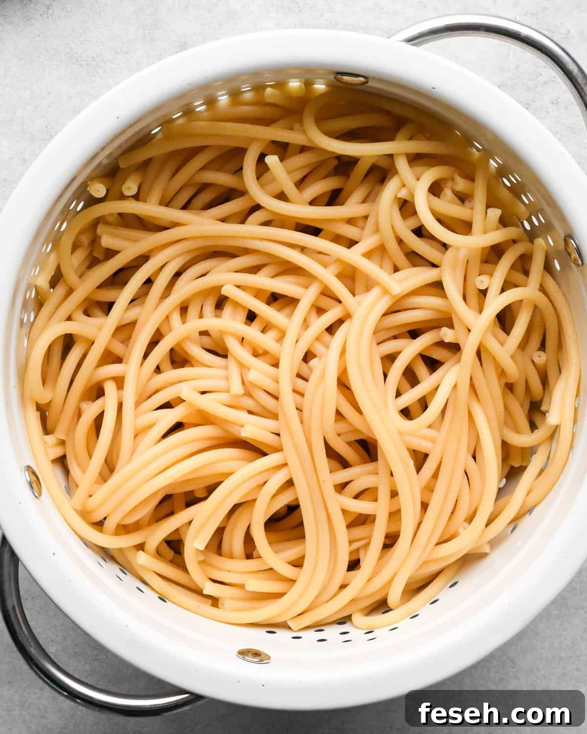 cooked pasta in a white colander with silver handles making pesto pasta