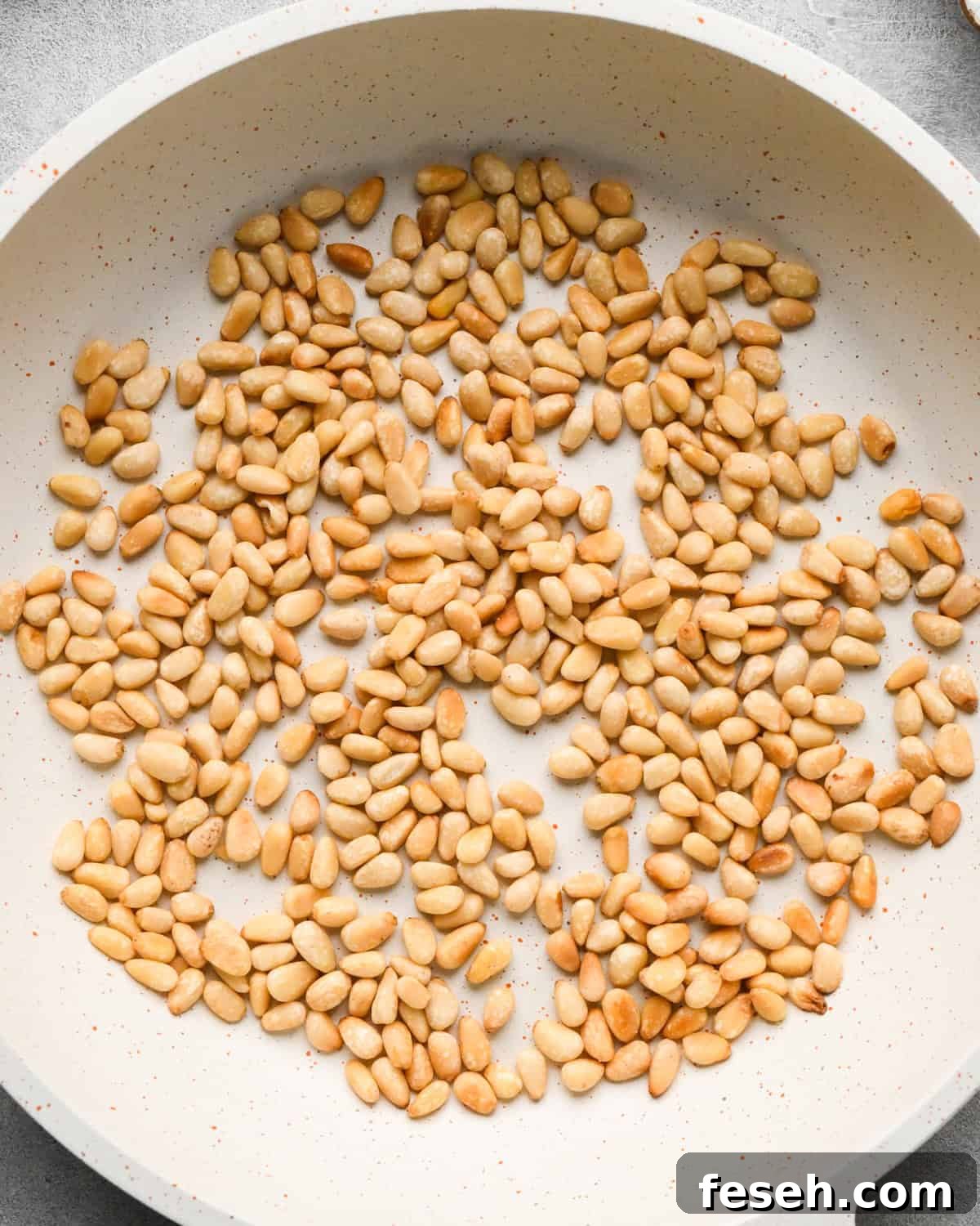 toasted pine nuts in a small, white skillet making this pesto and pasta recipe
