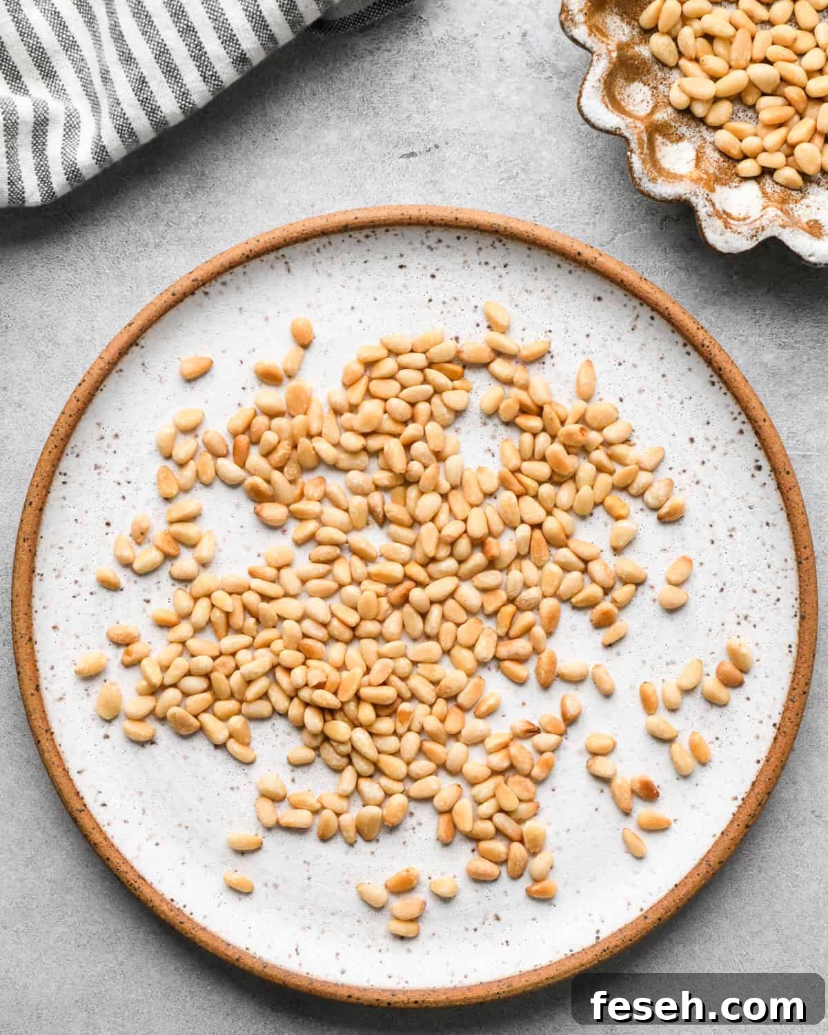 toasted pine nuts on a ceramic plate and in a ceramic bowl to be used to make this pesto pasta recipe
