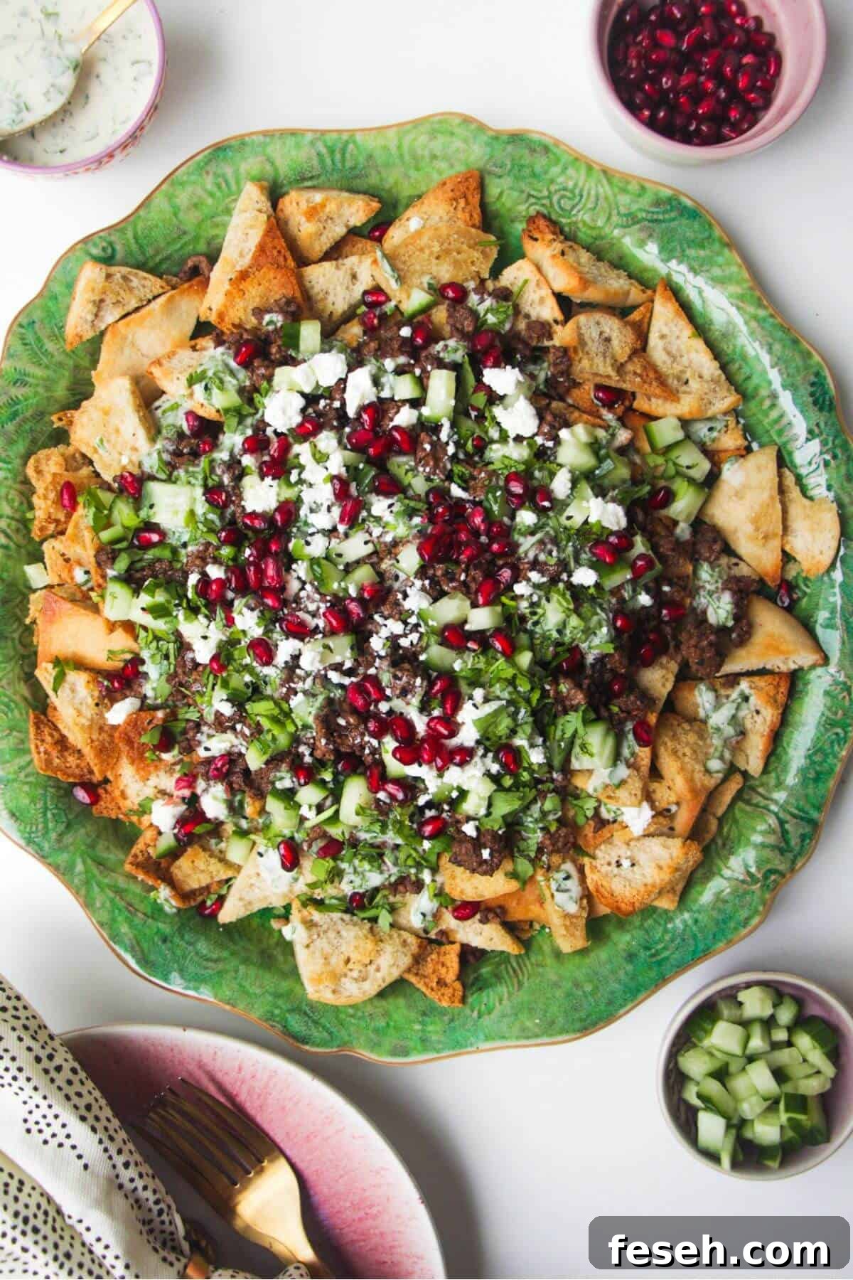 Middle Eastern style nachos on a green plate, with cucumber on the side.