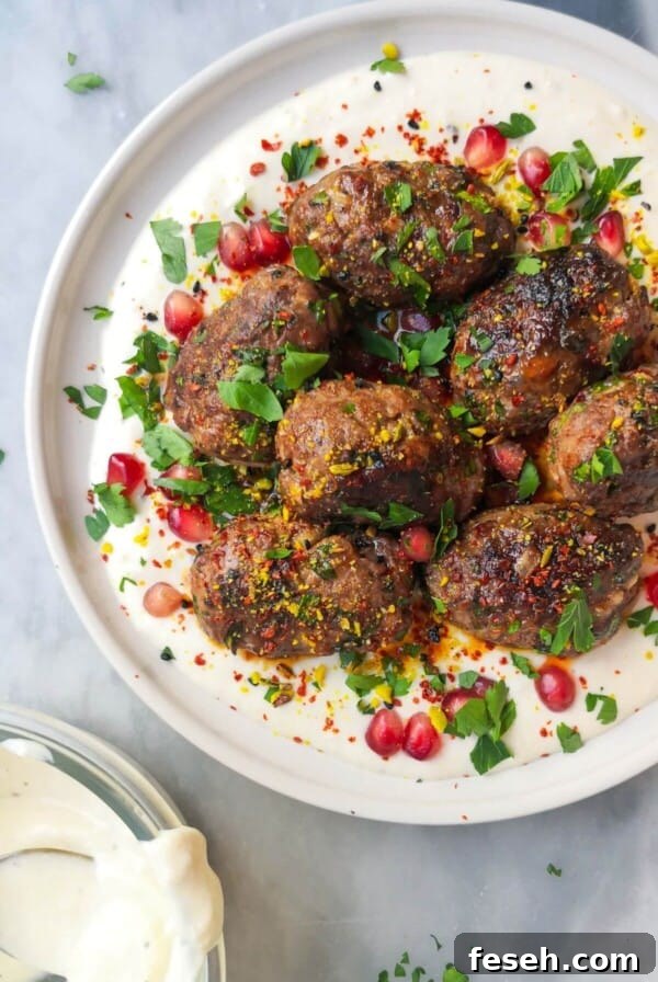 Lamb kofta with parsley, pomegranate seeds and dukkah on a white plate with yogurt tahini sauce, with a bowl of yogurt tahini sauce on the side.