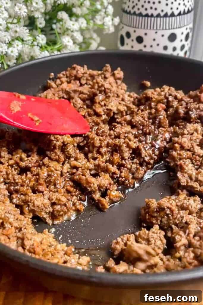 Spatula stirring sticky ground beef in a pan.