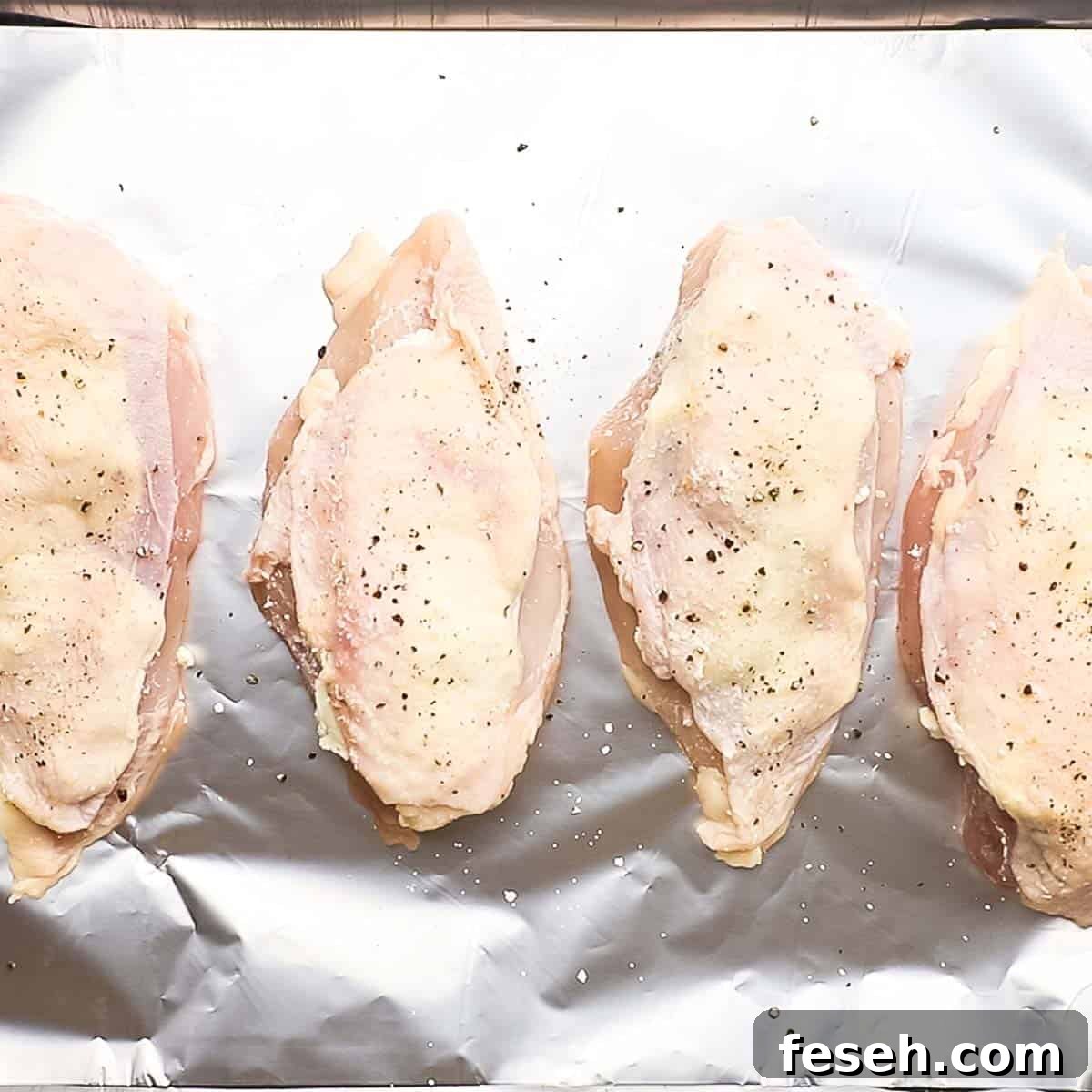 stuffed and seasoned chicken breasts placed on a baking sheet lined with aluminium