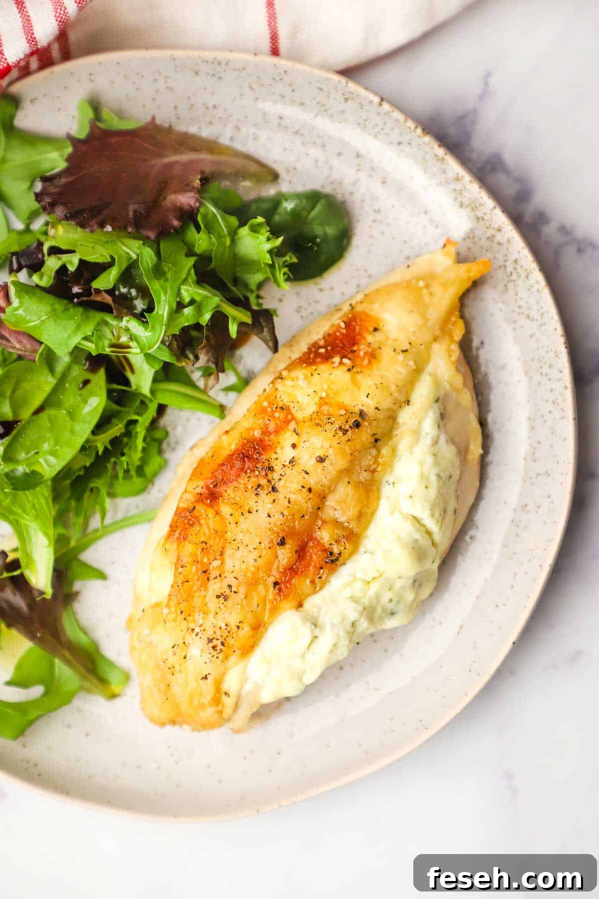 Overhead view of a Boursin-Stuffed Chicken breast on a plate with salad on the side.