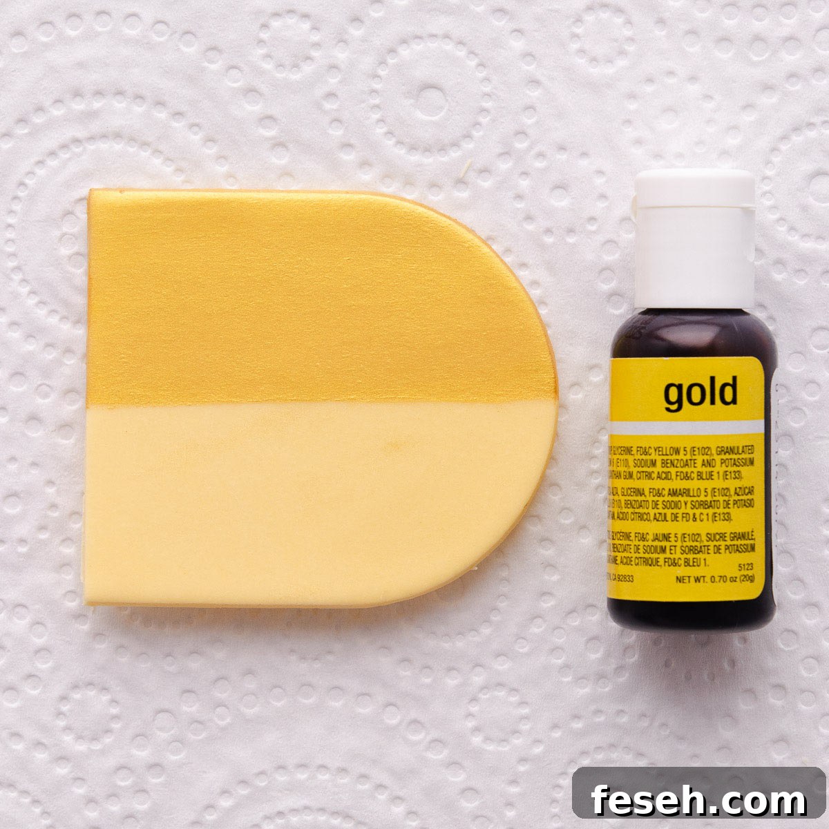 A small bottle of gold gel food colouring on a grey marble background.