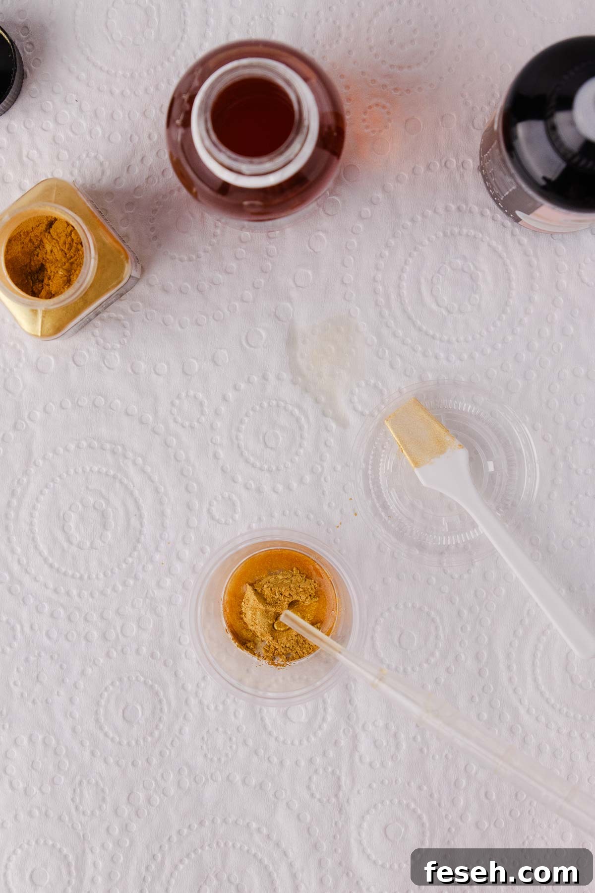A small dropper adding edible glaze to gold powder in a container.