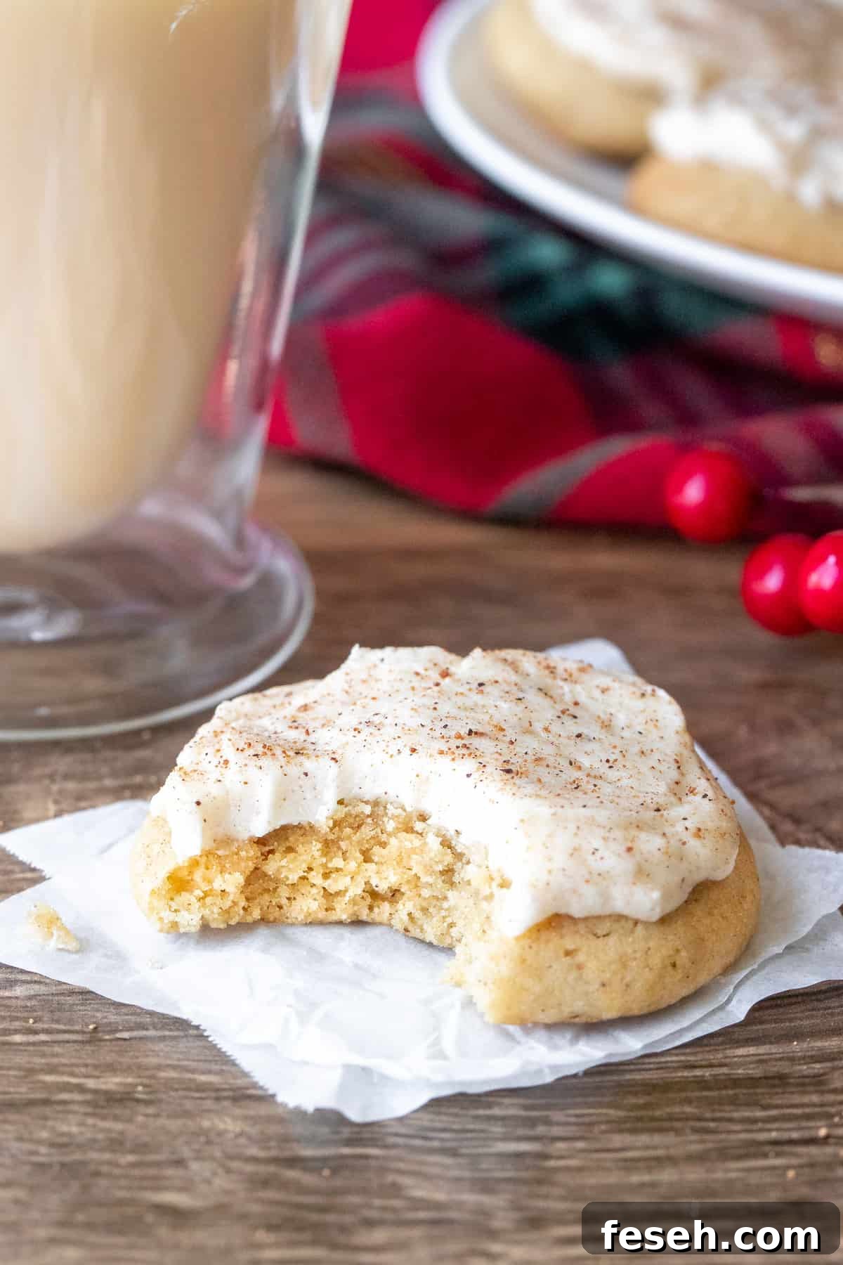 Holiday Eggnog Cookies with Creamy Eggnog Frosting 3 Frosted eggnog cookie with a bite taken out beside a glass of eggnog