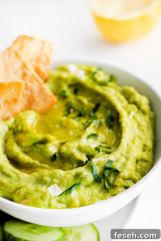 Creamy Avocado Hummus Recipe 3 white bowl filled with green avocado hummus and surrounded by chips and veggies