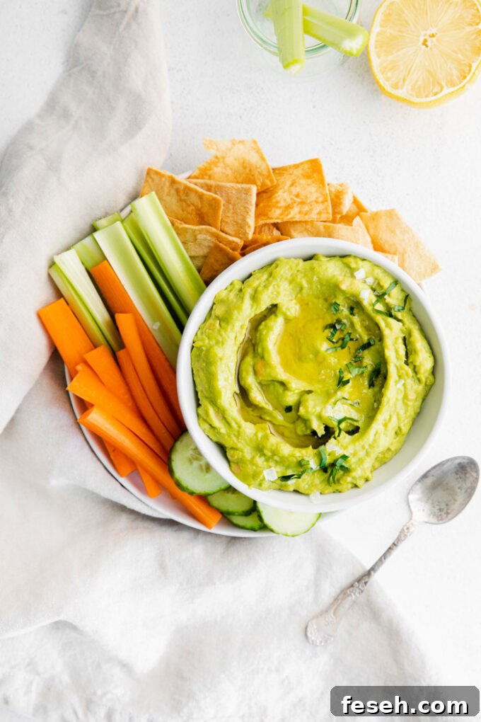 Creamy Avocado Hummus Recipe 4 white bowl filled with green avocado hummus and surrounded by chips and veggies