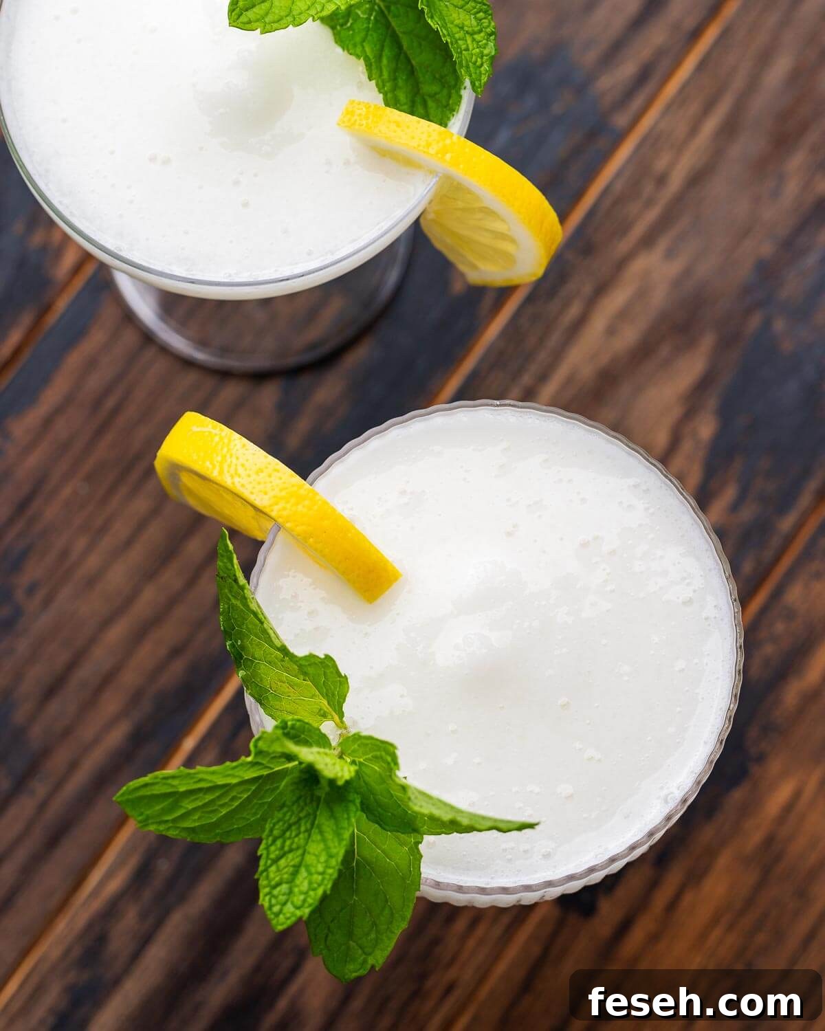 Sgroppino: Italian Lemon Sorbet and Prosecco Cocktail 4 Overhead shot of two glasses with sgroppino cocktail garnished with lemon wedges and mint on top of a wood table.