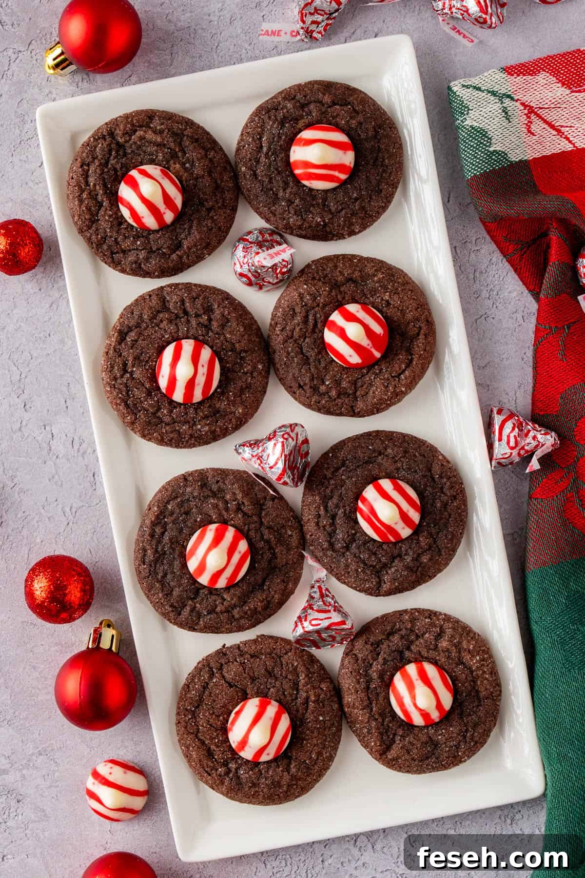 Chocolate Kiss Cookies with Hershey Candy Cane Kisses 2 Chocolate Kiss Cookies With Hershey's Candy Cane Kisses on a serving plate with wrapped candy cane kisses and red Christmas balls