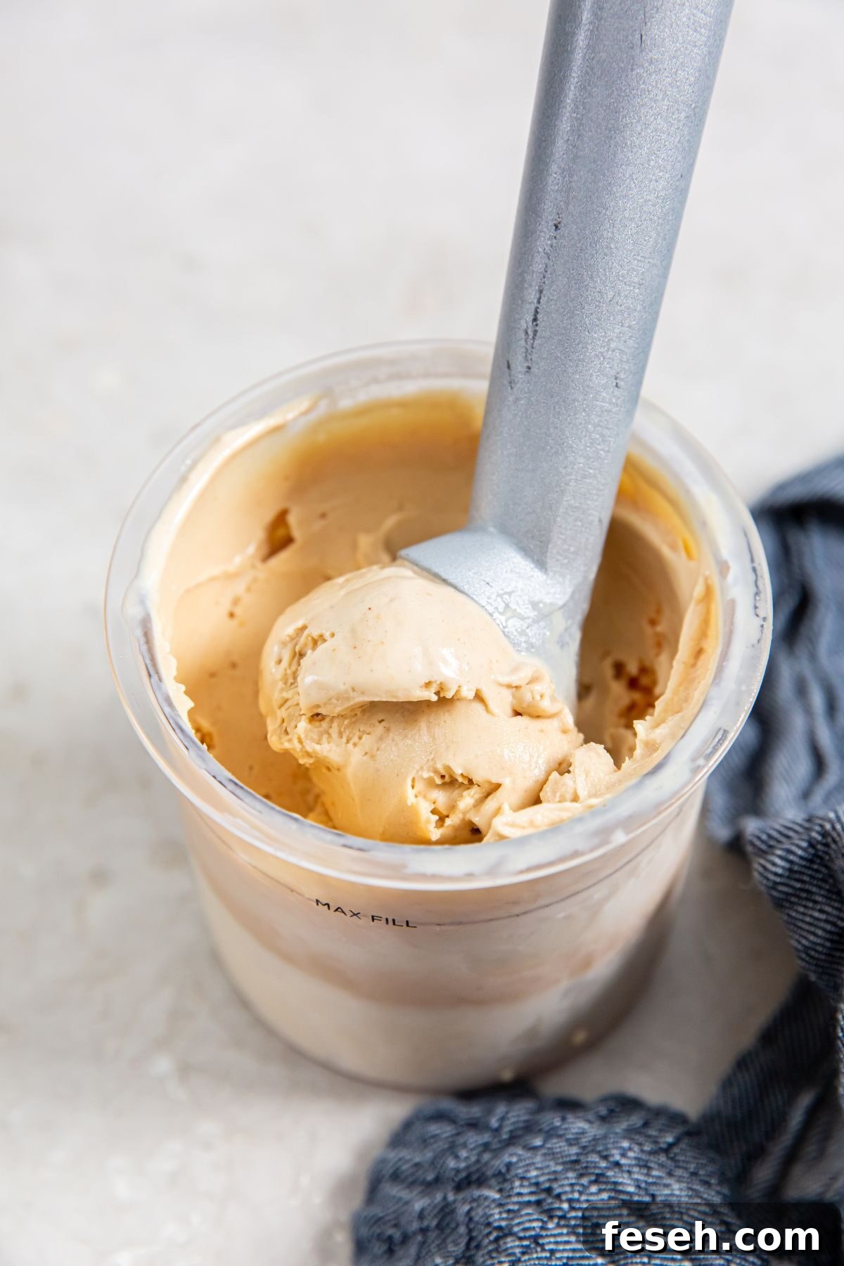 Ninja Creami Peanut Butter Ice Cream Recipe 2 Peanut butter ice cream in pint container with ice cream scoop next to a blue napkin