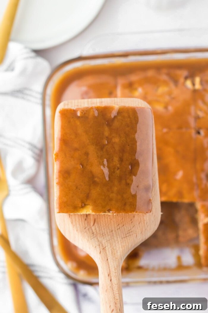 Moist Vegan Apple Cake with Cinnamon Glaze 12 A large wooden spatula with a square of caramel glazed apple cake on it held over the cake it was removed from in a glass baking dish.