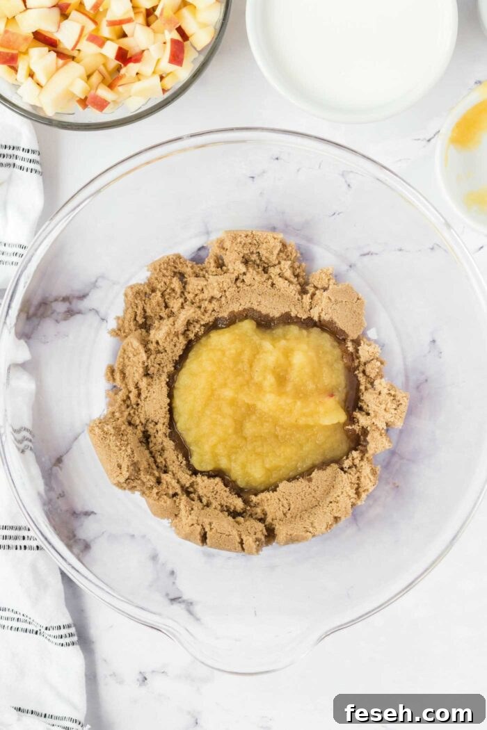 Moist Vegan Apple Cake with Cinnamon Glaze 4 Light brown sugar and applesauce in a glass mixing bowl. There are bowls of diced apple and milk beside the mixing bowl.