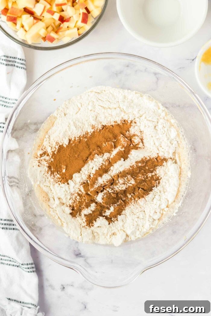 Moist Vegan Apple Cake with Cinnamon Glaze 6 Flour, cinnamon and baking powder added to a glass mixing bowl with cake batter in it.