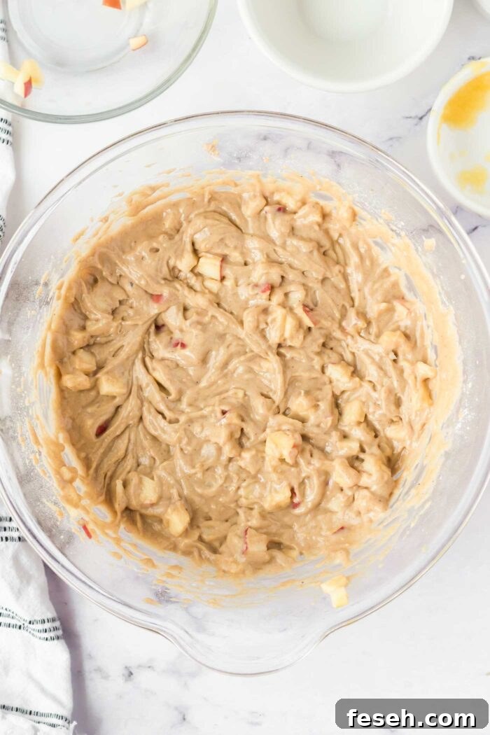 Moist Vegan Apple Cake with Cinnamon Glaze 7 Raw apple cake batter with pieces of diced apple in a large glass mixing bowl.
