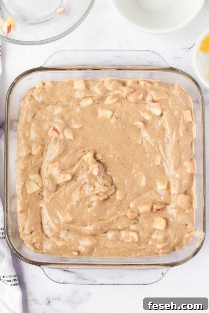 Moist Vegan Apple Cake with Cinnamon Glaze 8 Raw apple cake batter with pieces of apple in it in a square glass baking dish.