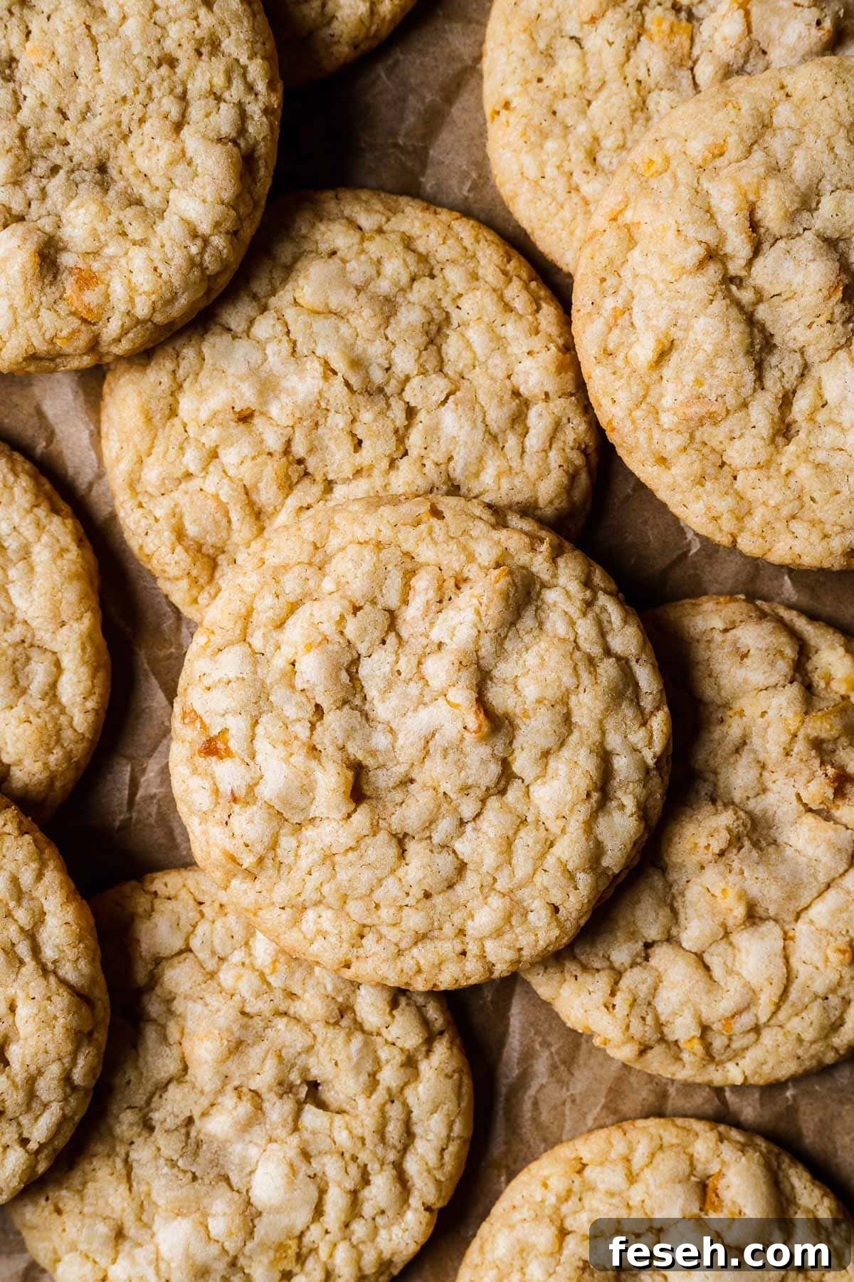 Tropical Mango Cookies with Coconut Glaze 12 Golden brown cookies piled on brown parchment paper.
