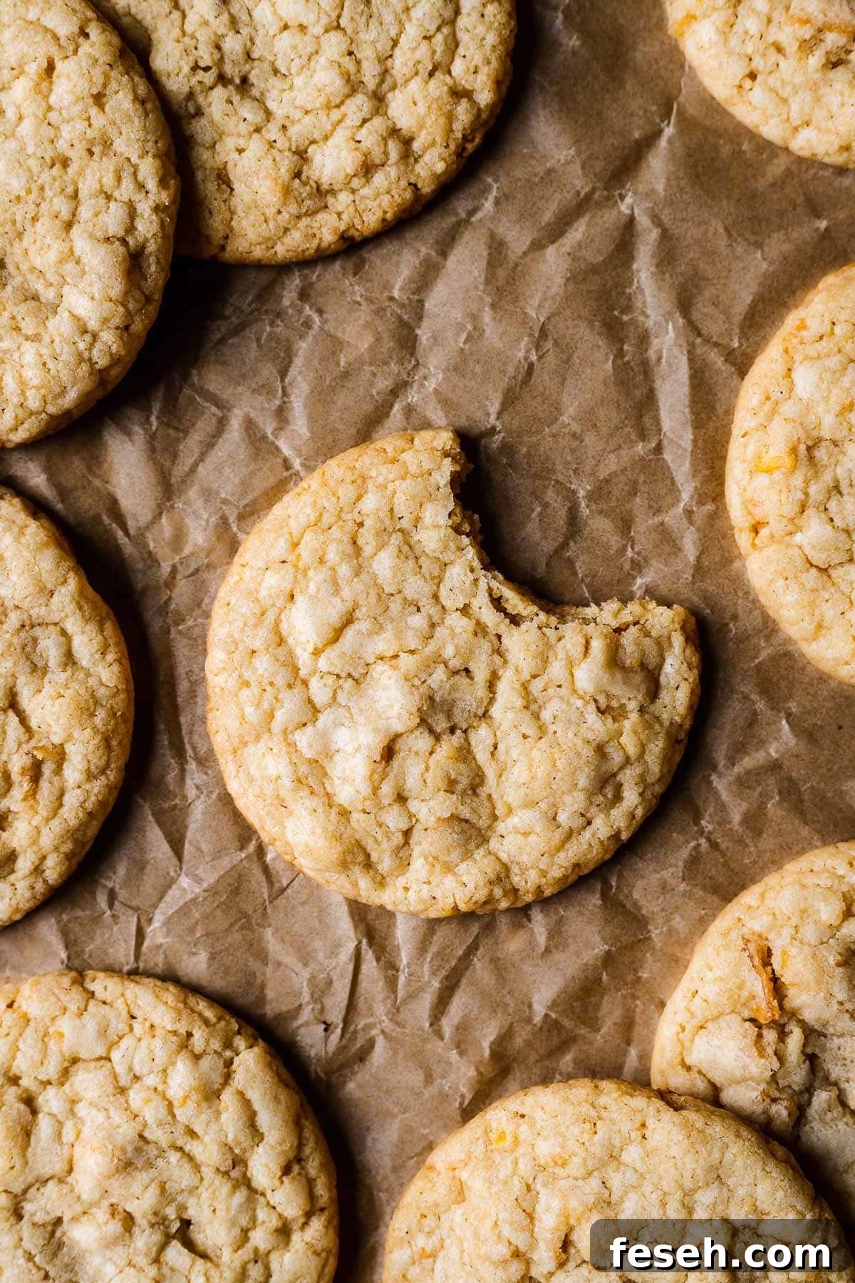 Tropical Mango Cookies with Coconut Glaze 13 A cookie on brown parchmenet with one bite taken out of it. More cookies peek into the frame.